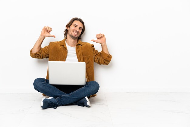 Hombre joven con su computadora portátil sentado en el suelo orgulloso y satisfecho de sí mismo