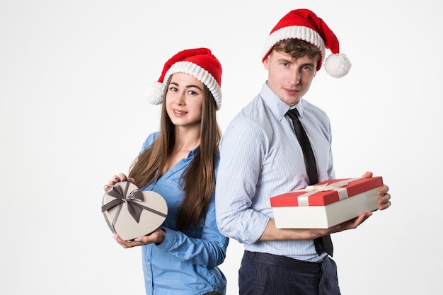 Hombre joven y su novia con sombrero de Santa con regalos sobre fondo blanco. Celebración de Navidad.