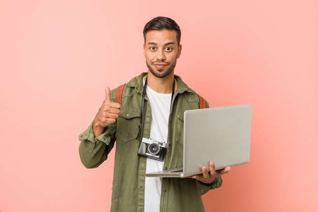 Hombre joven del sur de Asia que sostiene una computadora portátil.