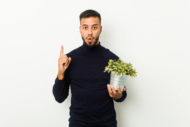 Hombre joven del sur de Asia que sostiene una planta que tiene una gran idea