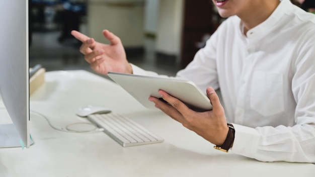 Hombre joven con tableta digital y videoconferencia con una computadora para la reunión en línea desde casa, trabajar desde casa, trabajar en línea.