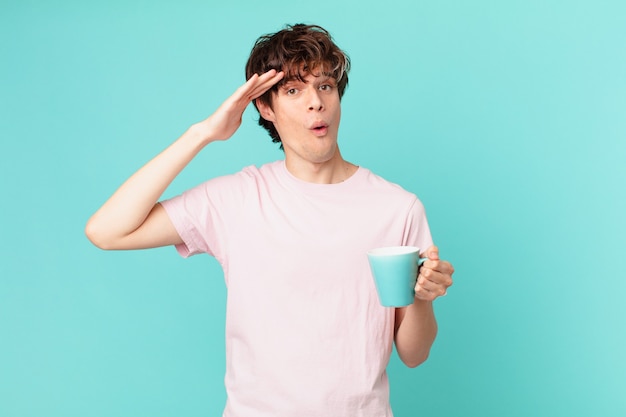 Hombre joven con una taza de café mirando feliz, asombrado y sorprendido