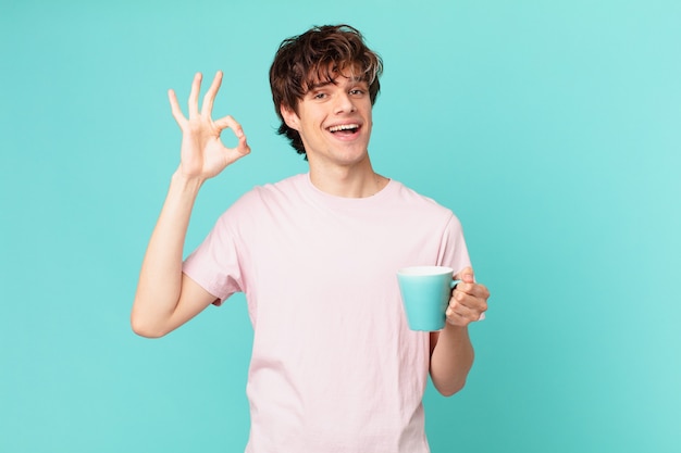 Hombre joven con una taza de café sintiéndose feliz, mostrando aprobación con gesto bien