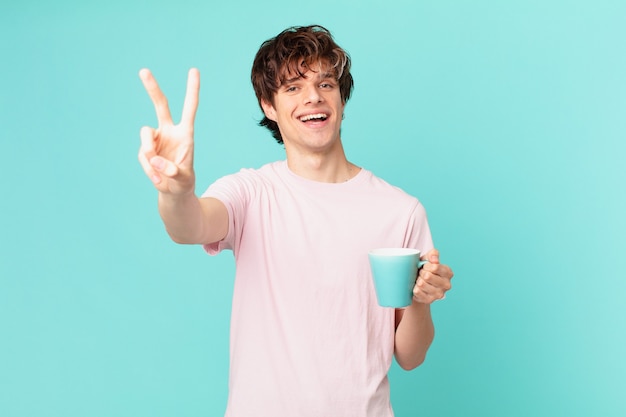 Hombre joven con una taza de café sonriendo y mirando feliz, gesticulando victoria o paz