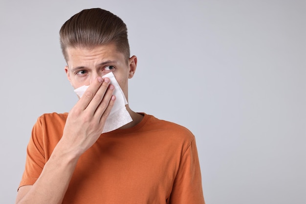 Hombre joven con tejido que sufre de sinusitis en un espacio de fondo gris claro para el texto