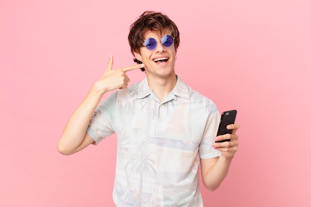 Hombre joven con un teléfono celular sonriendo con confianza apuntando a su propia amplia sonrisa