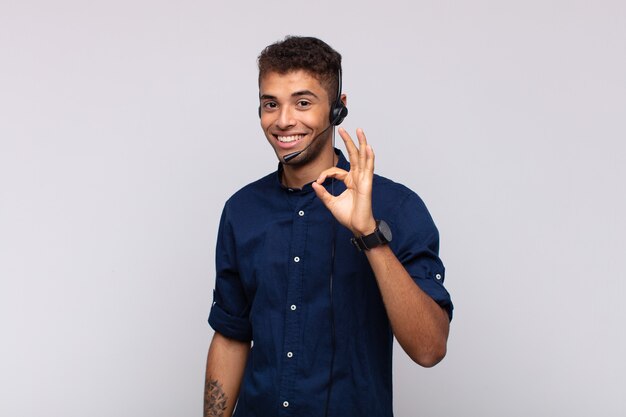 Hombre joven de telemercadeo que se siente feliz, relajado y satisfecho, mostrando aprobación con gesto bien, sonriendo