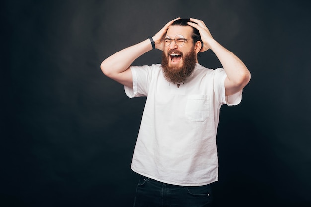 El hombre joven se toca la cabeza y grita con los ojos cerrados.