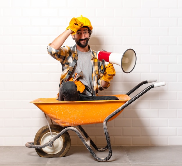 Hombre joven trabajador de la construcción barbudo en una carretilla de mano