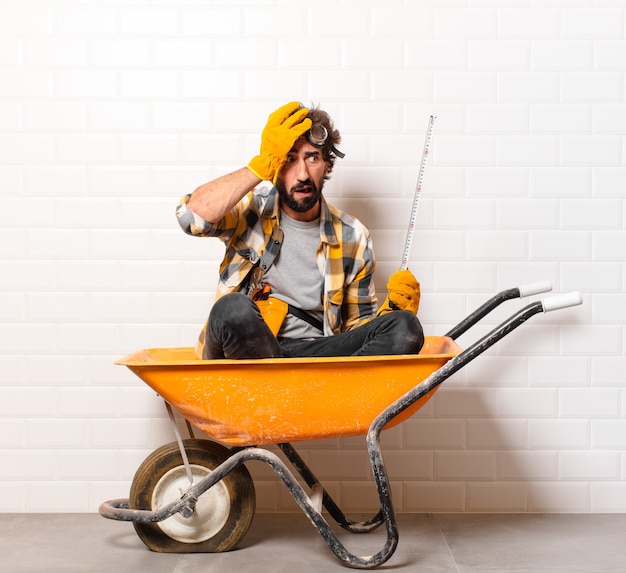 Hombre joven trabajador de la construcción barbudo en una carretilla de mano