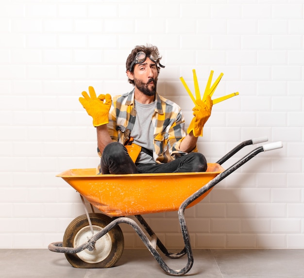 Hombre joven trabajador de la construcción barbudo en una carretilla de mano