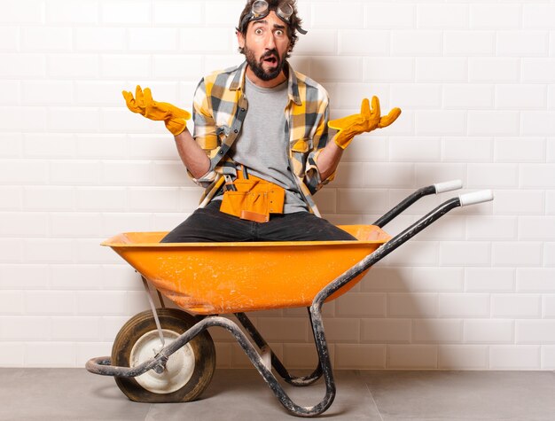 Hombre joven trabajador de la construcción barbudo en una carretilla de mano