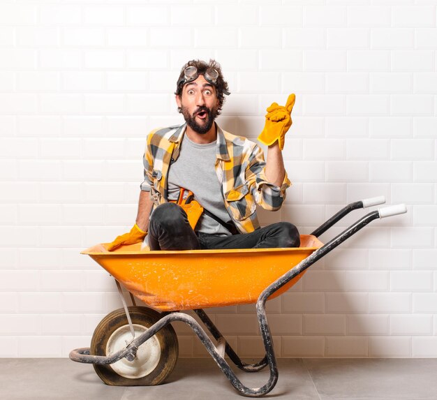 Hombre joven trabajador de la construcción barbudo en una carretilla de mano