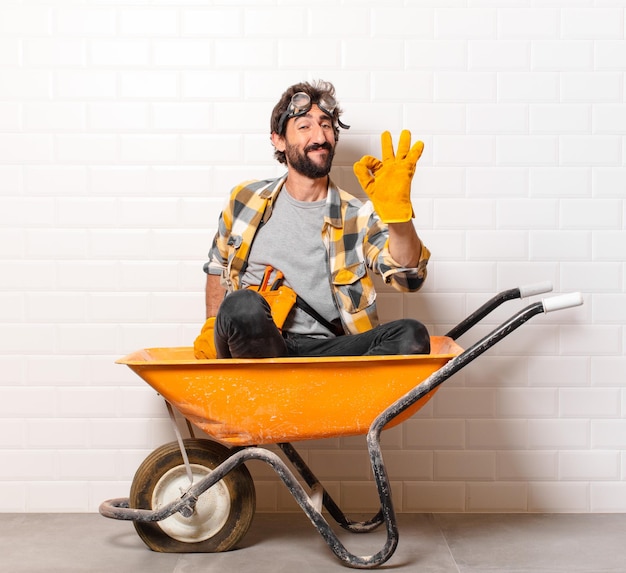 Hombre joven trabajador de la construcción barbudo en una carretilla