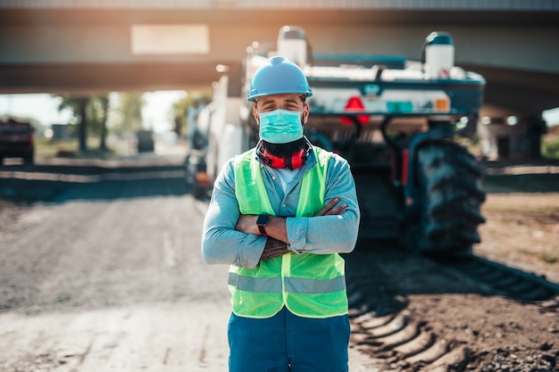 Hombre joven trabajador de la construcción de carreteras con máscara protectora en su trabajo. Día soleado. Luz fuerte.