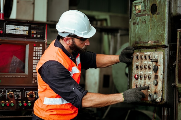 Hombre joven trabajador industrial que trabaja con la máquina de metal en la fábrica con muchos equipos