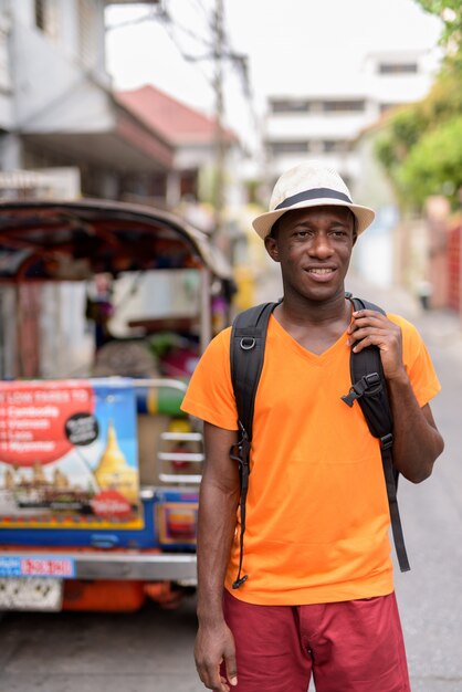 Hombre joven turista feliz sonriendo y pensando mientras sostiene la mochila en las calles de Bangkok, Tailandia