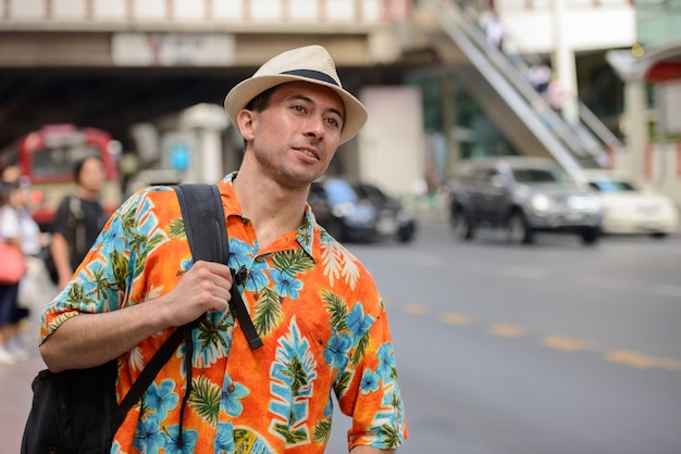 Hombre joven turista guapo con mochila pensando en las calles de la ciudad