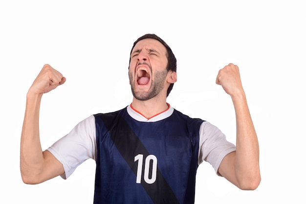 Hombre joven en uniforme del fútbol del fútbol que grita mientras que su equipo gana.