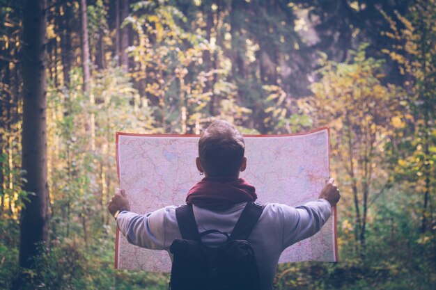 Hombre joven del viajero con el mapa, mochila en el bosque del verde del otoño en día soleado.