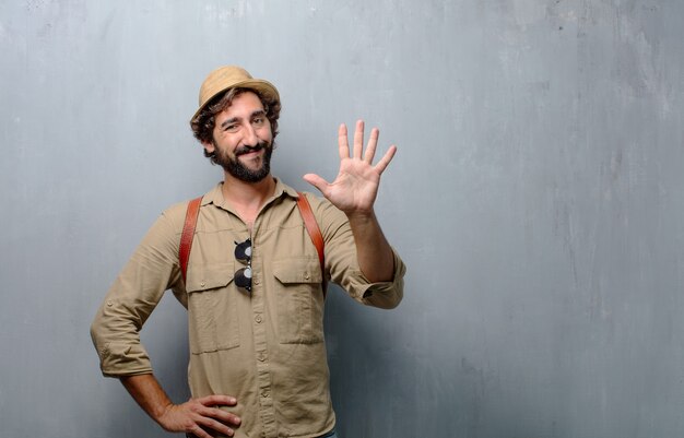 Hombre joven viajero o turista sonriendo, contando el número cinco con los dedos, con la palma abierta.