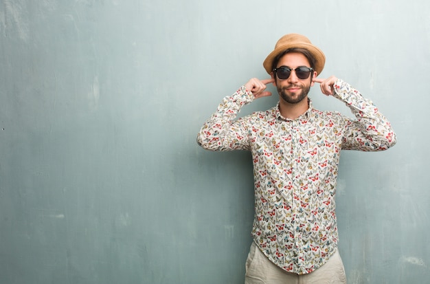 Hombre joven del viajero que lleva una camisa colorida que cubre los oídos con las manos