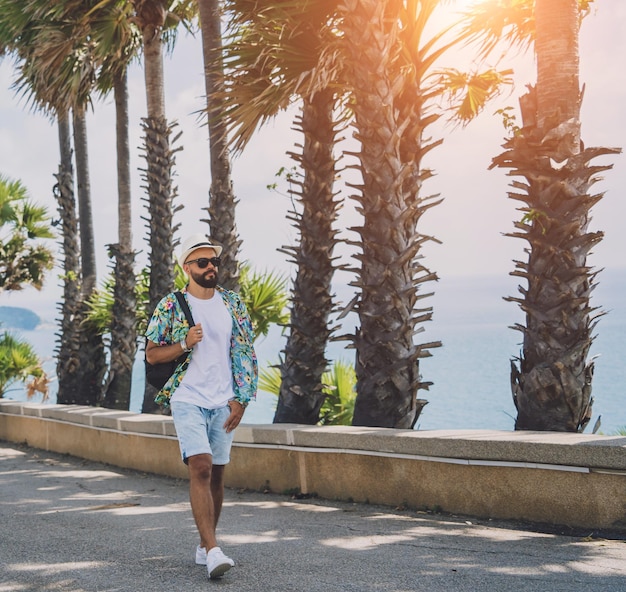 Hombre joven viajero en vacaciones de verano con hermosas palmeras y paisajes marinos en el fondo