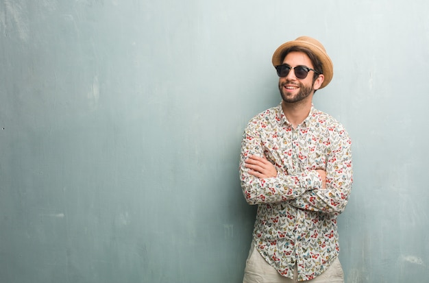 Hombre joven viajero vistiendo una camisa colorida mirando hacia arriba, pensando en algo divertido y teniendo una idea