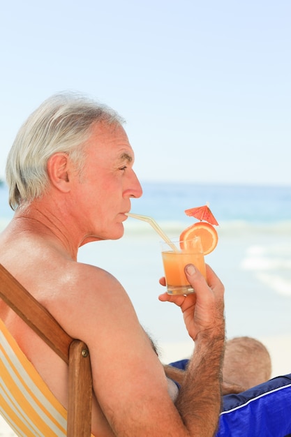 Hombre jubilado bebiendo un cóctel en la playa