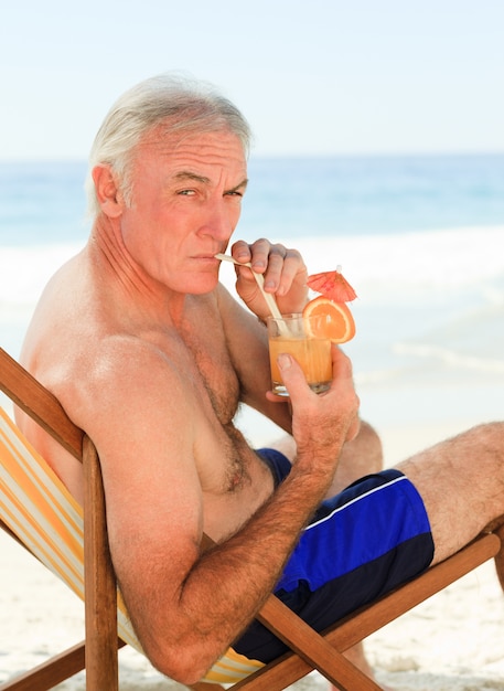 Hombre jubilado bebiendo un cóctel en la playa