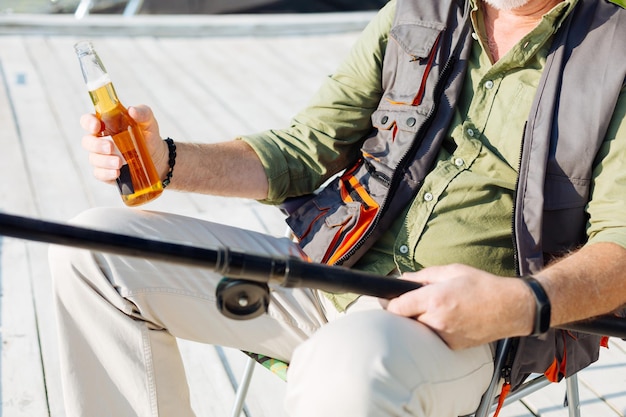 Hombre jubilado con chaleco bebiendo cerveza y pescando el fin de semana