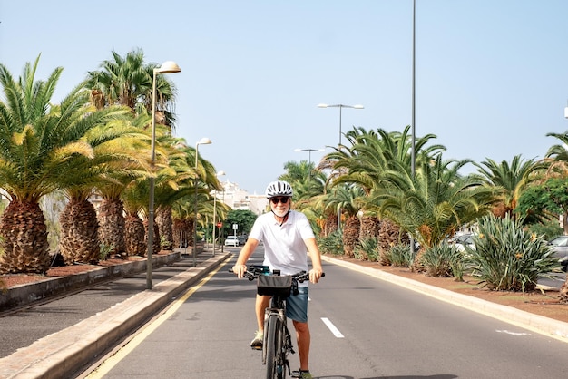 Hombre jubilado feliz disfrutando de la actividad corriendo con su bicicleta eléctrica en una calle soleada de la ciudad