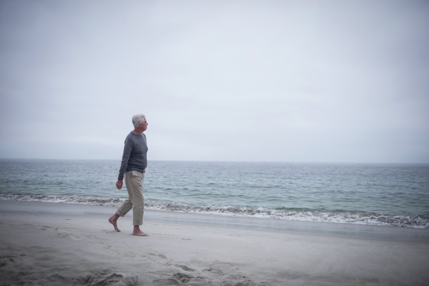 Hombre jubilado pensativo caminando por la playa