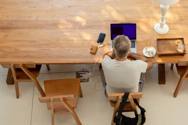 Hombre jubilado que trabaja en la computadora portátil con una taza de café en la mesa.