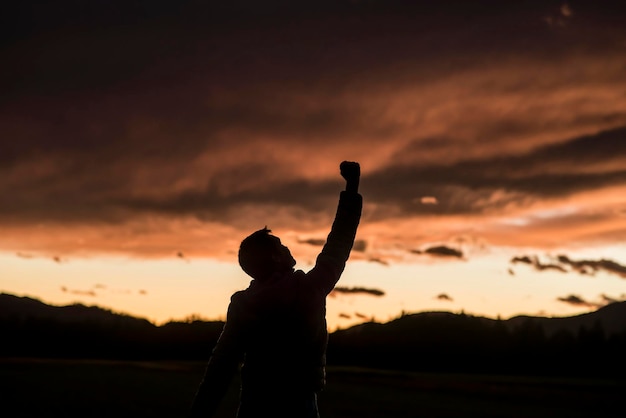 Hombre jubiloso levantando su puño contra una puesta de sol