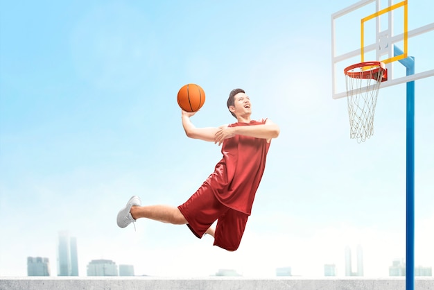 Hombre de jugador de baloncesto asiático salta en el aire con la pelota tratando de anotar