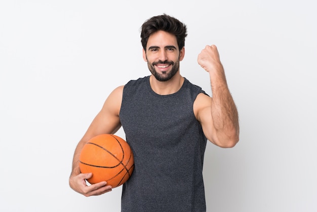 Hombre de jugador de baloncesto con barba sobre pared blanca aislada celebrando una victoria