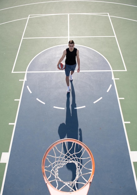 Hombre jugador de baloncesto deportista en camisa y pantalones cortos sostienen pelota de baloncesto sobre fondo urbano Concepto de motivación deportiva