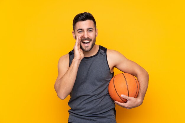 Hombre de jugador de baloncesto joven guapo sobre pared blanca aislada gritando con la boca abierta