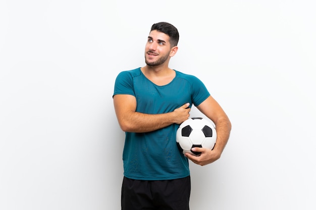 Hombre de jugador de fútbol joven guapo sobre pared blanca aislada mirando hacia arriba mientras sonríe