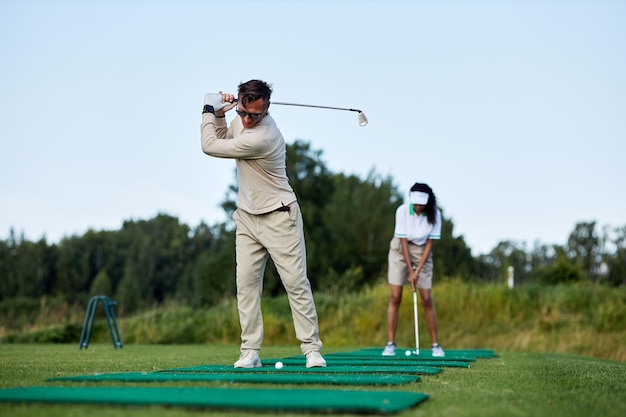 Hombre jugando al golf y al club de balanceo mientras está de pie en la plataforma