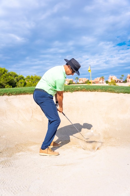 Hombre jugando al golf en el búnker golpeando la pelota con la cuña de lanzamiento de palo