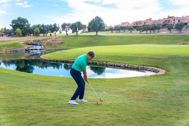 Hombre jugando al golf en el club de golf junto a un lago golpeando la pelota con la plancha o lanzando