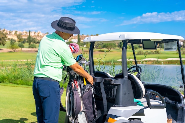 Hombre jugando al golf recogiendo el palo después del lanzamiento en la bolsa del palo y colocándolo en el buggy