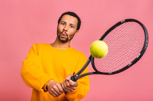 hombre jugando al tenis aislado sobre rosa. Foto de estudio de joven jugador en forma en el estudio en movimiento o movimiento durante el juego deportivo.