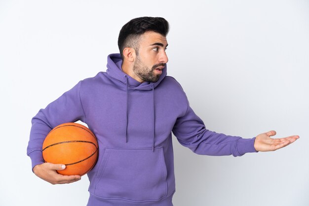 Hombre jugando baloncesto sobre pared blanca aislada con expresión de sorpresa mientras mira de lado