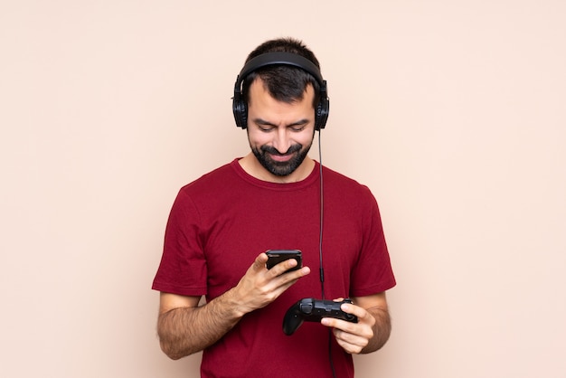 Hombre jugando con un controlador de videojuego sobre una pared aislada enviando un mensaje con el móvil