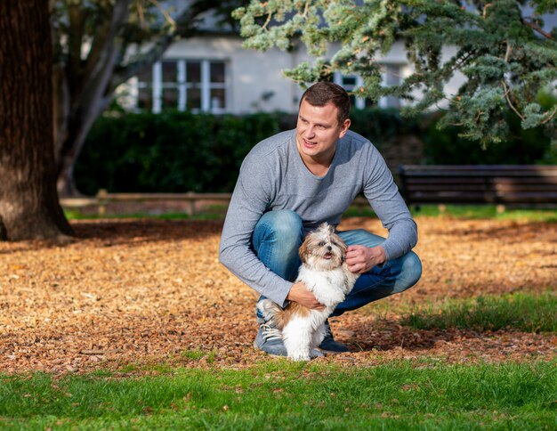 Hombre jugando con shih tzu cachorro al aire libre, adiestramiento de perros en el parque