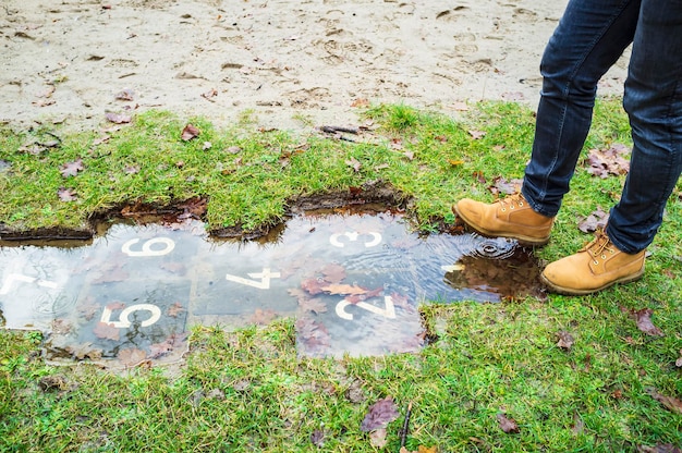 Foto hombre va a jugar a la rayuela y saltar en cuadrados con números inundados de agua durante un deshielo