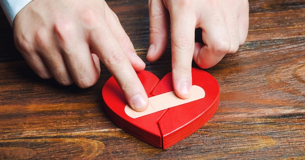 Foto un hombre junta un corazón rojo con un yeso.